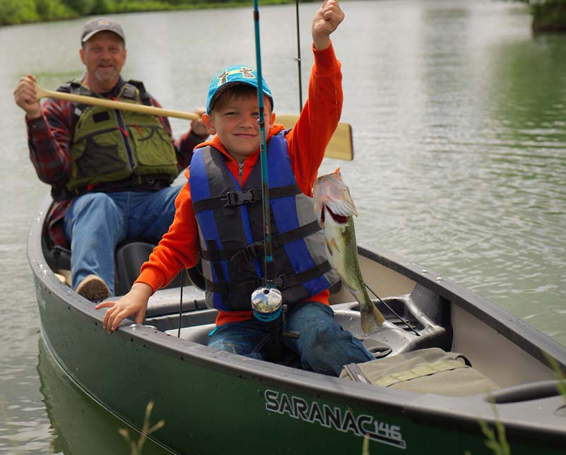 Child holding up caught fish on hook while paddling with Grandpa in Old Town Saranac Canoe