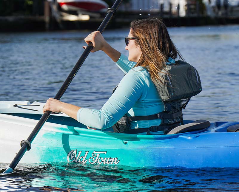 Woman paddling in Old Town Vapor kayak wearing Solitude II Life Jacket