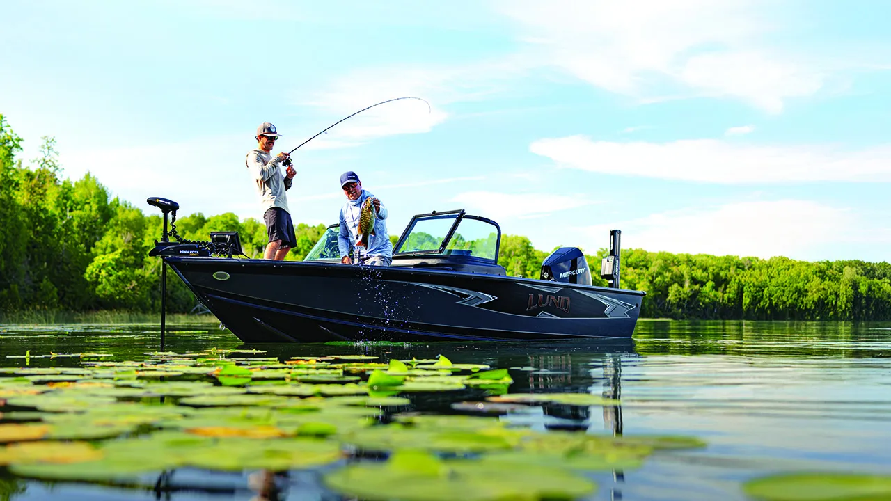 A male angler sets the hook on a weedy bass pond, while standing on a fishing boat.
